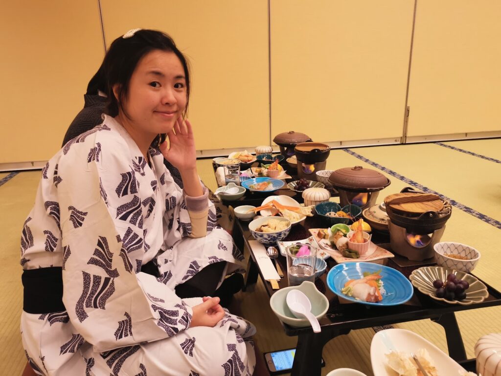 Staying at a Ryokan in Japan With Kids: What to Expect 9 Woman wearing a yukata sitting on tatami floor enjoying a traditional Japanese kaiseki meal at a ryokan.