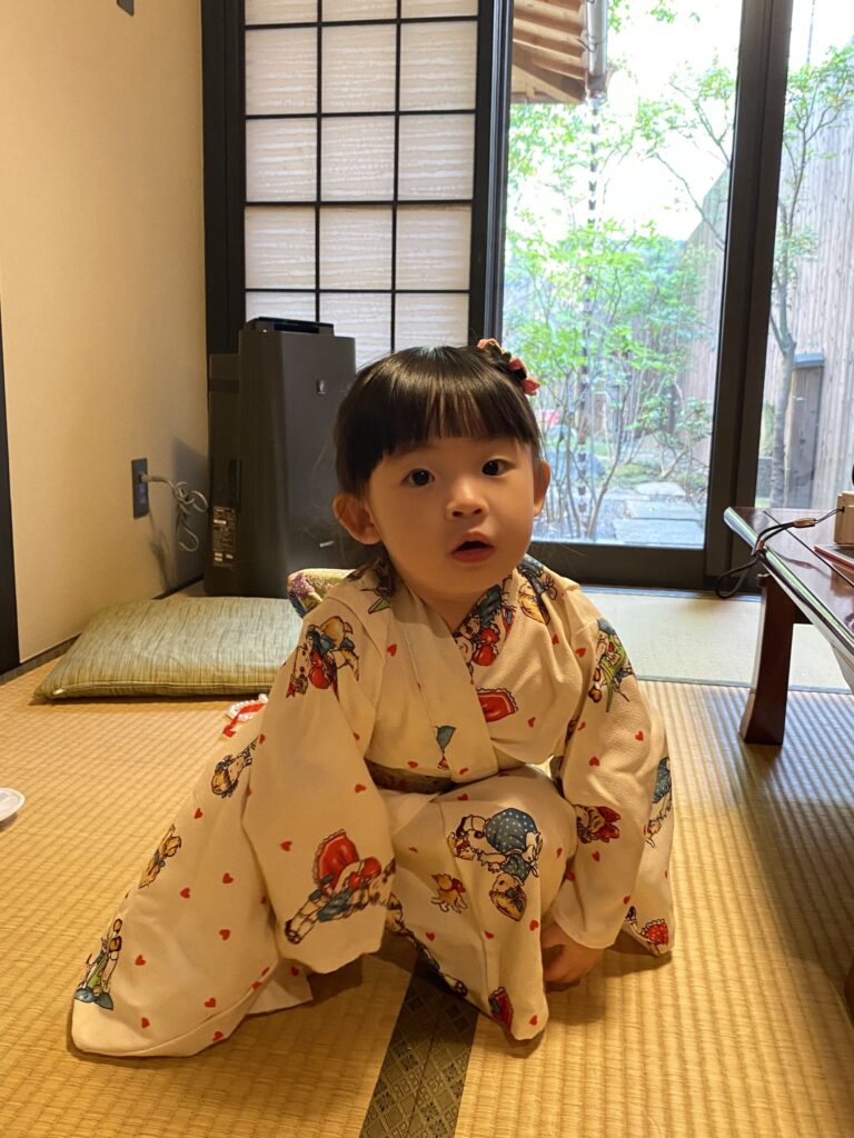 Staying at a Ryokan in Japan With Kids: What to Expect 6 Toddler wearing a colorful yukata sitting on a tatami floor in a traditional Japanese ryokan room.
