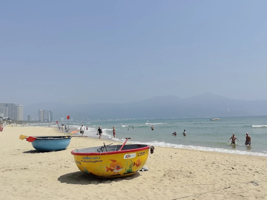 Traditional Vietnamese basket boats on My Khe Beach Da Nang with people swimming in the sea