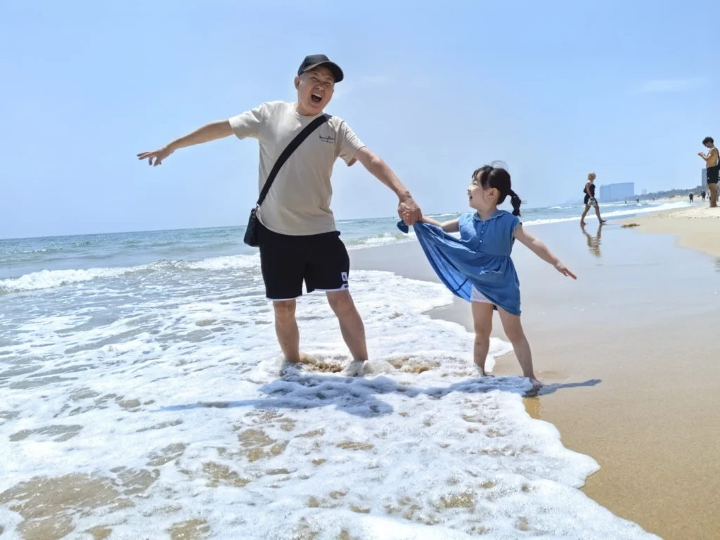 Grandfather and daughter playing in the waves at My Khe Beach Da Nang Vietnam