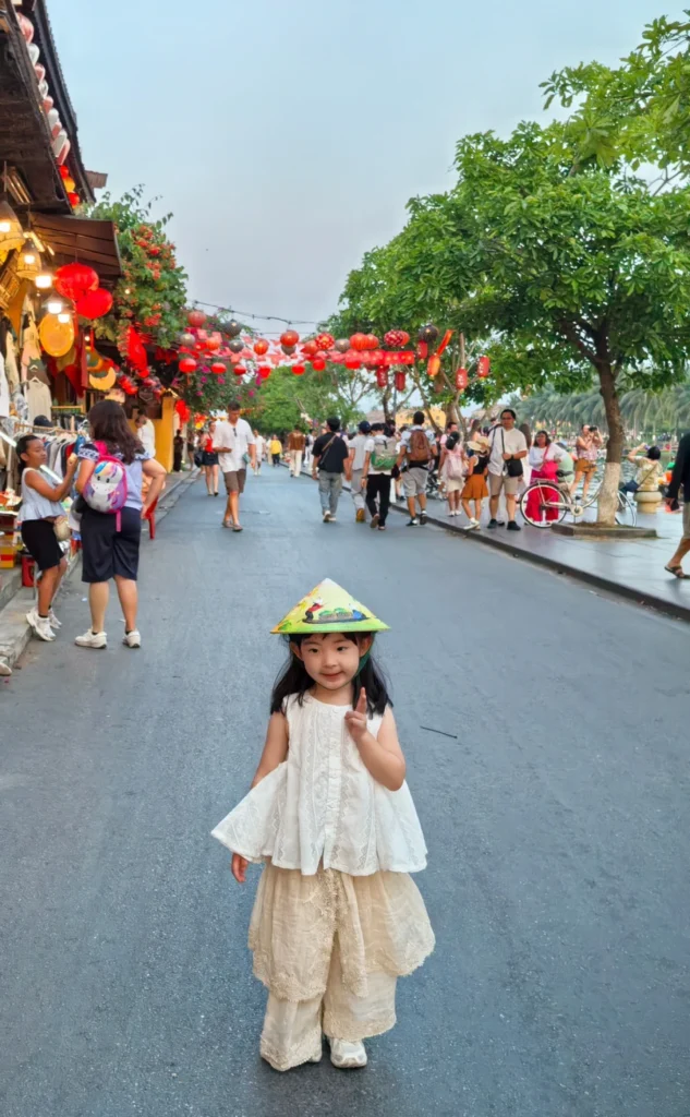 Child wearing traditional conical hat walking along lantern street in Hoi An Ancient Town