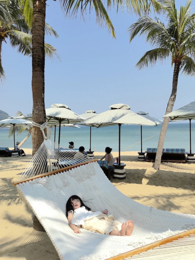 Child resting on hammock at private beach with palm trees at InterContinental Danang Sun Peninsula Resort