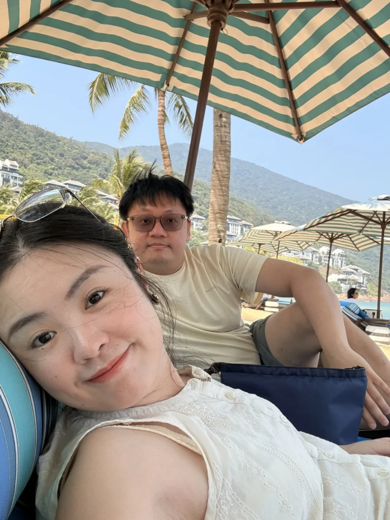 Couple relaxing on beach lounge chairs under umbrella at InterContinental Danang Sun Peninsula Resort