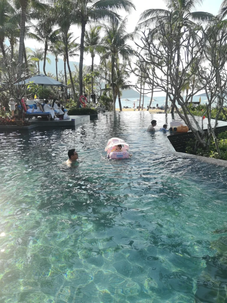 Family swimming in infinity pool with palm trees and beach view at InterContinental Danang Sun Peninsula Resort