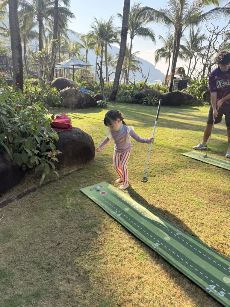 Child playing mini golf on lawn with tropical garden at InterContinental Danang Sun Peninsula Resort