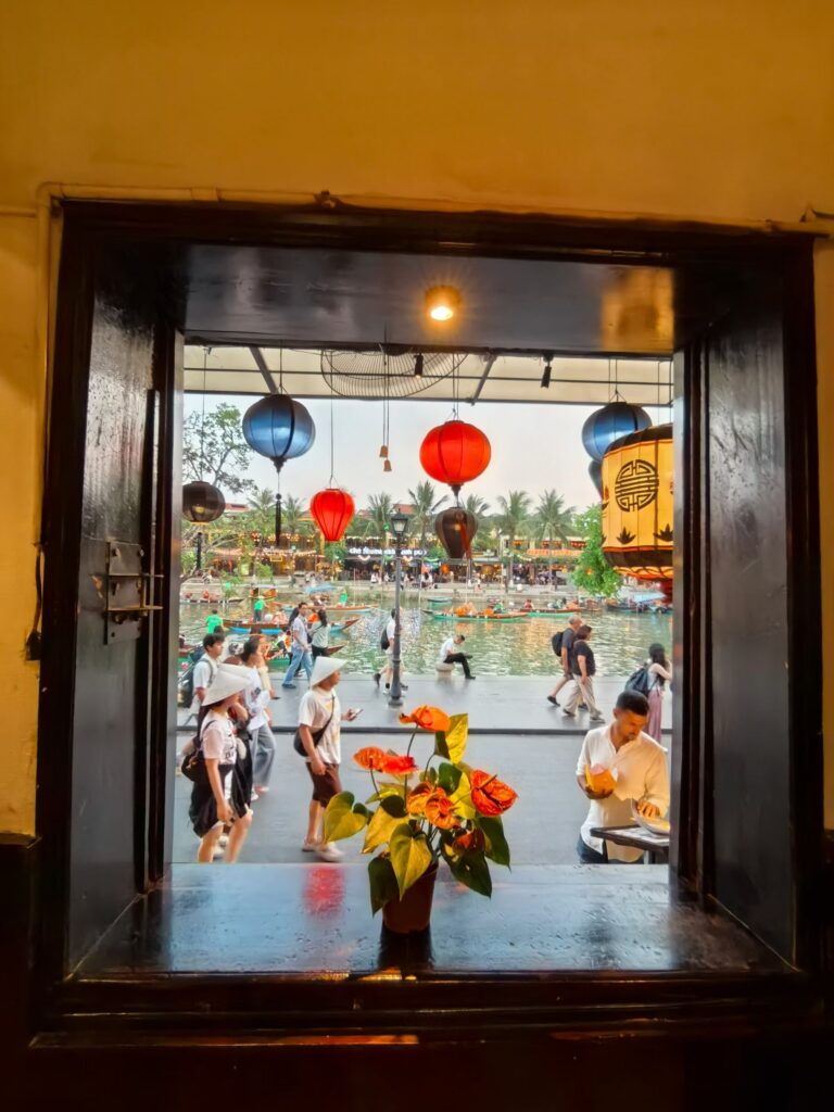 Hoi An riverside cafe window view with lanterns and street activity