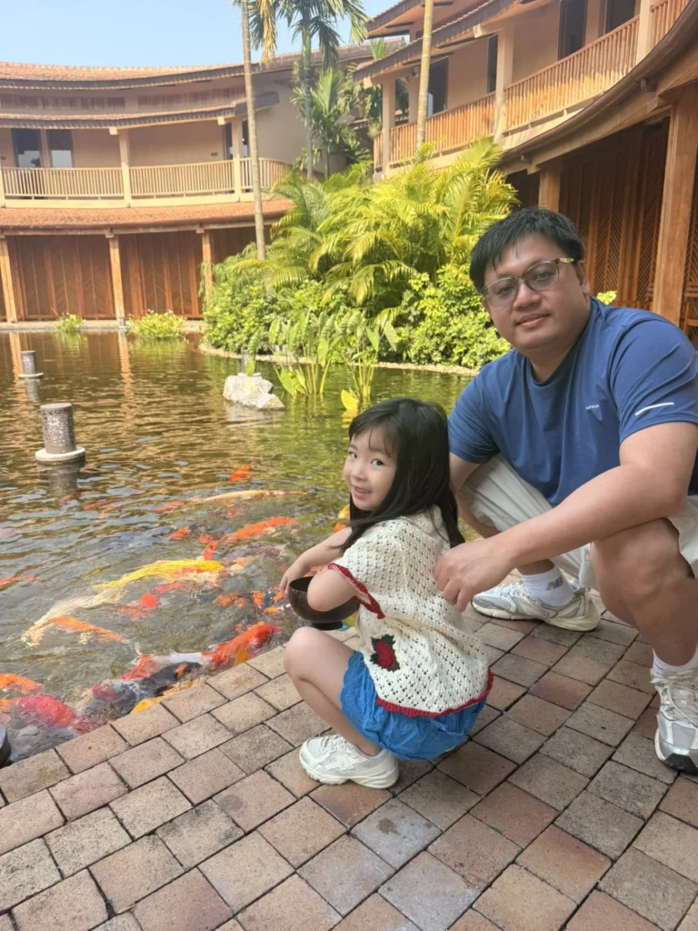 Father and daughter feeding koi fish at Namia River Retreat courtyard in Hoi An
