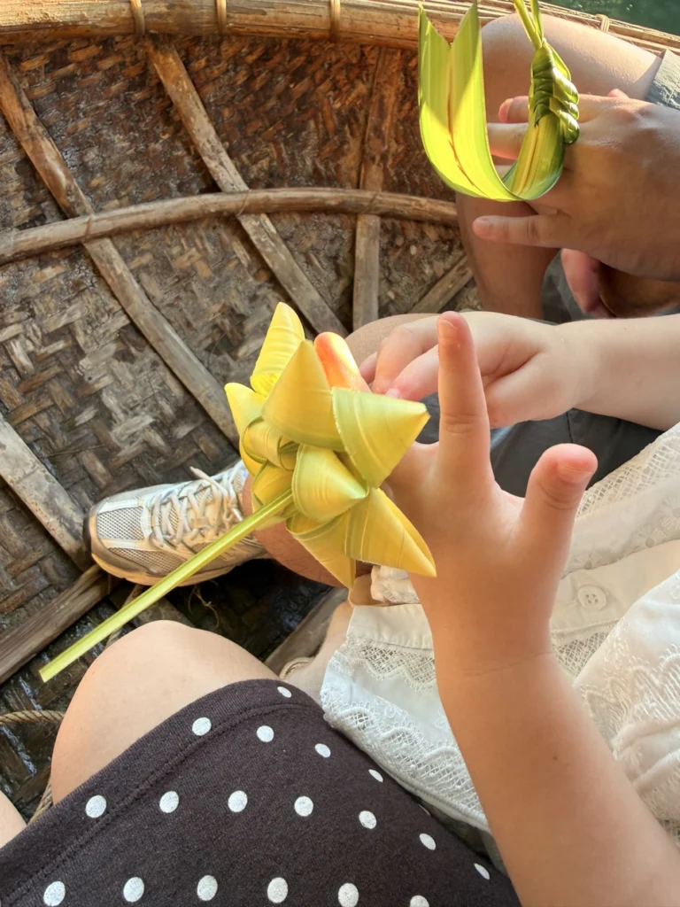 Child holding handmade palm leaf toy during basket boat ride in Hoi An