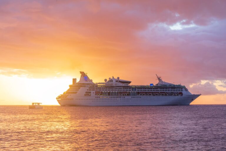 Cruise ship sailing across calm ocean waters during a vibrant sunset with orange and purple skies