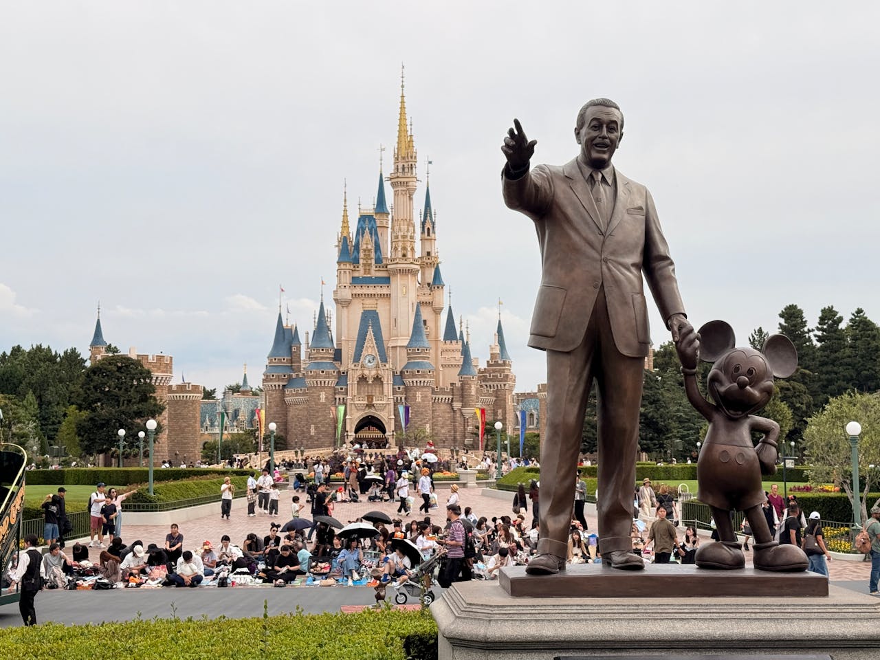 Statue of Walt Disney and Mickey Mouse in front of Cinderella Castle at Tokyo Disneyland with visitors gathered in the park