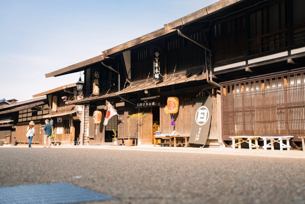 Staying at a Ryokan in Japan With Kids: What to Expect 5 Traditional Japanese wooden street with historic ryokan-style buildings, paper lanterns, and a Japanese flag, with people walking in the background.