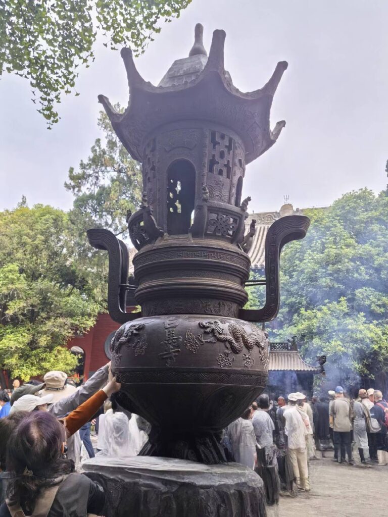 Large bronze incense burner at White Horse Temple with visitors offering incense