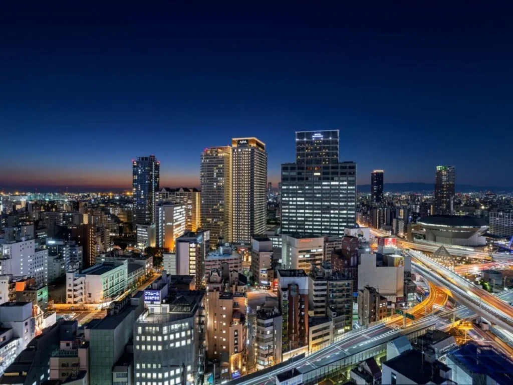 Osaka city skyline at night featuring APA Hotel & Resort Osaka Namba Ekimae Tower near Namba Station with illuminated highways and modern buildings