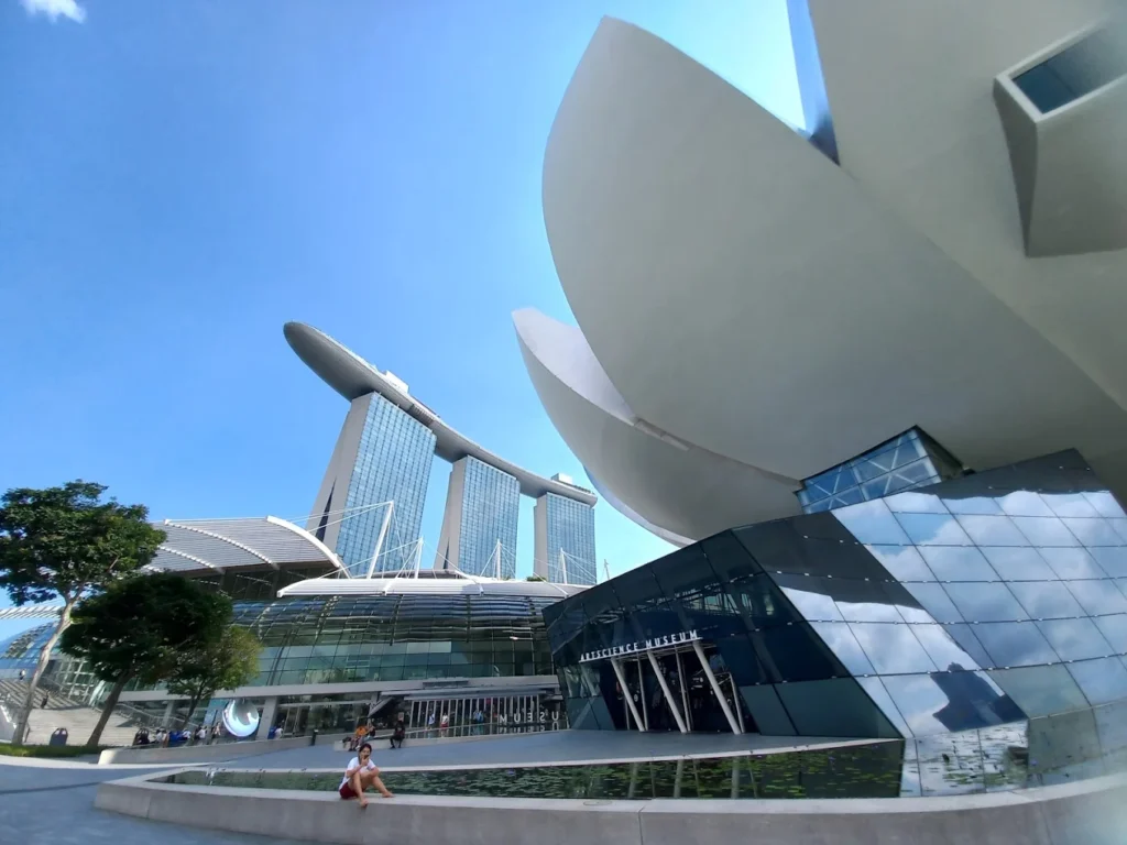 Wide-angle view of Singapore’s ArtScience Museum with Marina Bay Sands towering in the background on a bright sunny day.