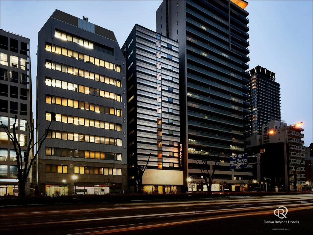 Nighttime exterior view of DEL Style Osaka Higashitemma, featuring a modern high-rise hotel building illuminated along a busy Osaka city street.