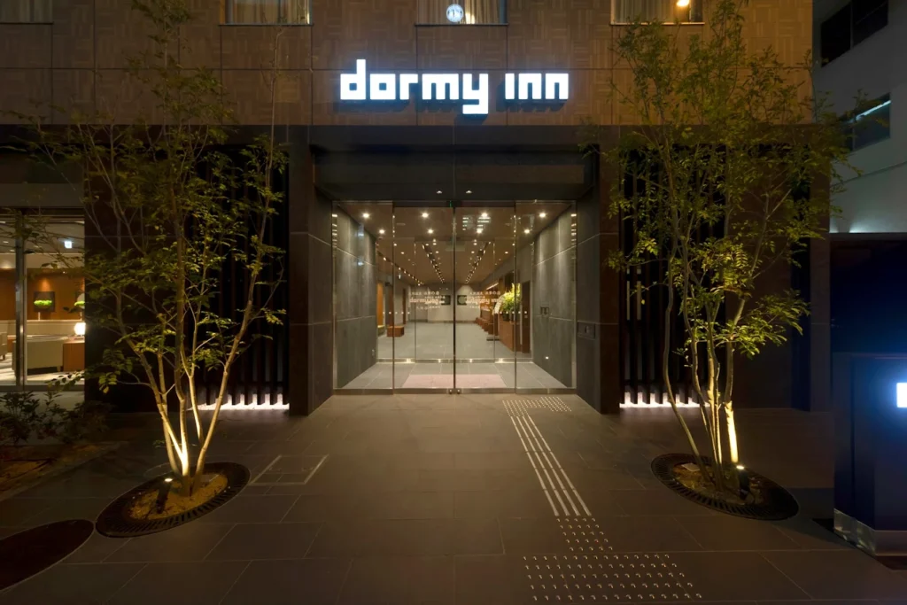 Entrance view of Dormy Inn Osaka Tanimachi at night, featuring a warmly lit modern hotel lobby with minimalist Japanese-style design and illuminated signage.