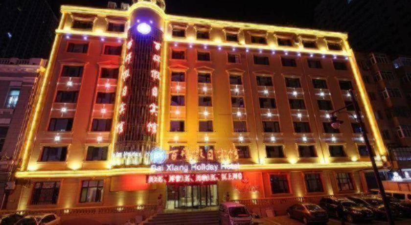 Harbin Baixiang Holiday Hotel illuminated at night with warm golden lights and classic European-style architecture in Harbin, China.