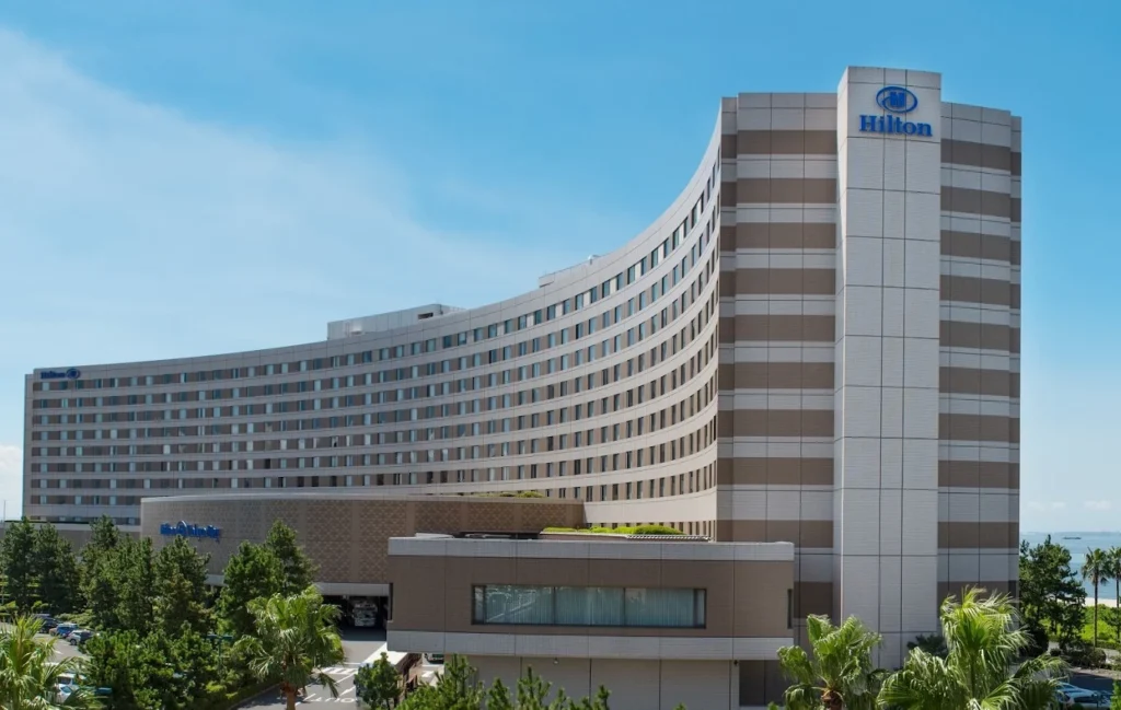 Exterior view of Hilton Tokyo Bay featuring its curved modern building design, surrounded by palm trees and resort landscaping near Tokyo DisneySea.