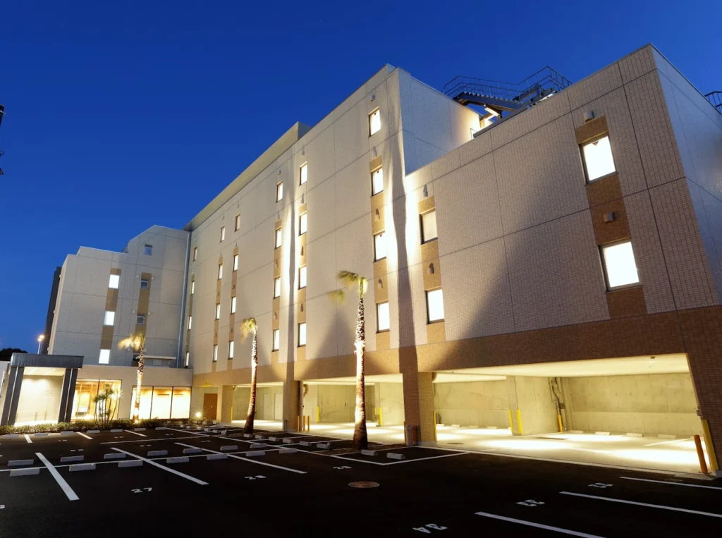 Evening exterior view of Hiyori Hotel Maihama with warm lighting, palm trees, and a modern minimalist facade near Tokyo DisneySea.