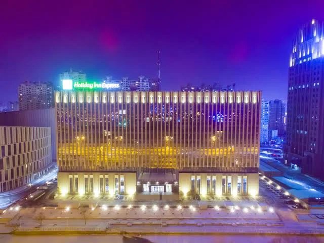 Holiday Inn Express Harbin Qunli illuminated at night with modern architecture and city skyline in Harbin, China.