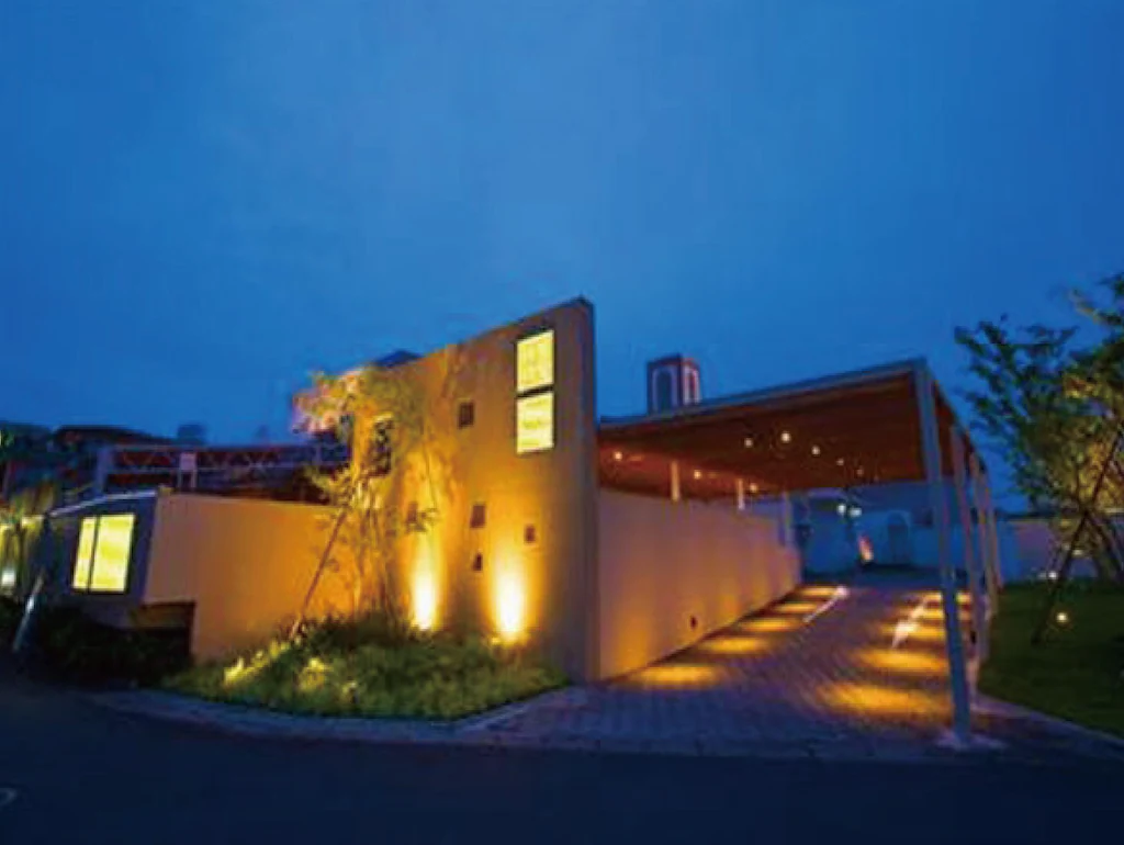 Exterior night view of Hotel Hug Hug Kyoto featuring warm ambient lighting, minimalist modern architecture, and a private driveway entrance in Kyoto, Japan.
