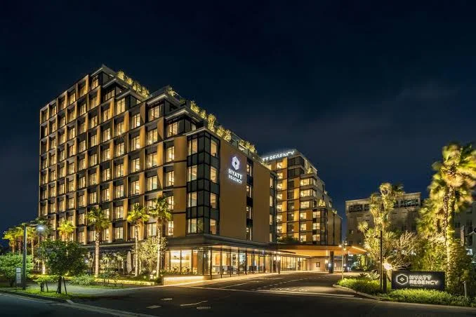 Nighttime exterior view of Hyatt Regency Tokyo Bay featuring modern architecture, warm lighting, palm trees, and landscaped grounds near Tokyo DisneySea.