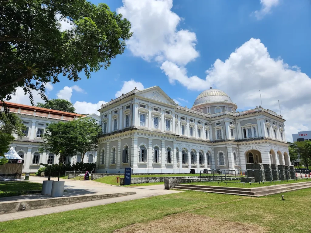 Exterior view of the National Museum of Singapore featuring its historic colonial-style architecture and dome under a blue sky.