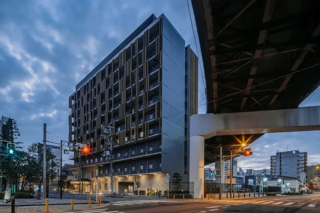 Exterior view of Nest Hotel Osaka Shinsaibashi near an elevated roadway in Osaka during early evening