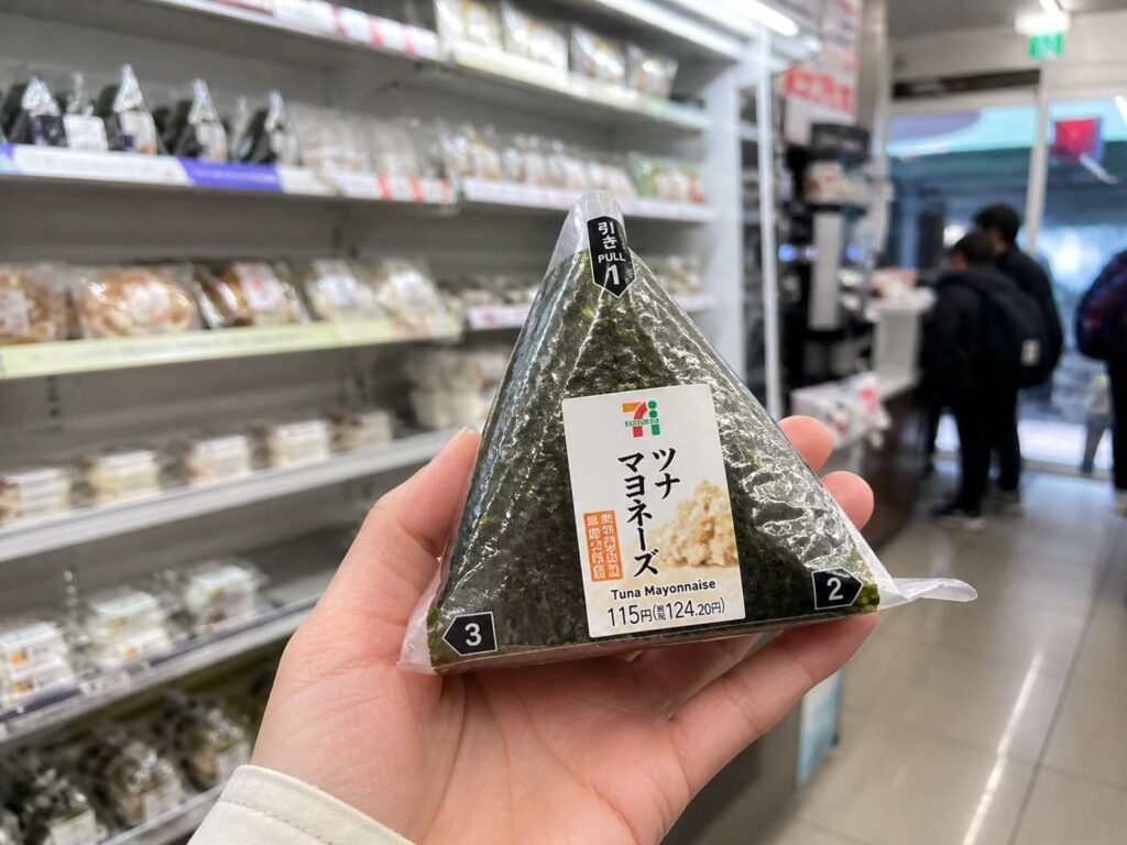 Kid-Friendly Foods to Try in Japan That Aren’t Sushi 10 Packaged onigiri rice ball held in hand inside a Japanese convenience store