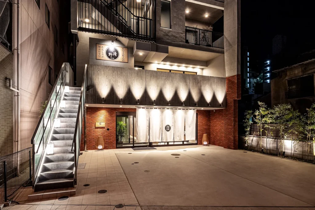 Nighttime exterior of PROSTYLE Ryokan Tokyo Asakusa featuring modern Japanese-inspired architecture and a traditional ryokan-style entrance near Asakusa Temple.