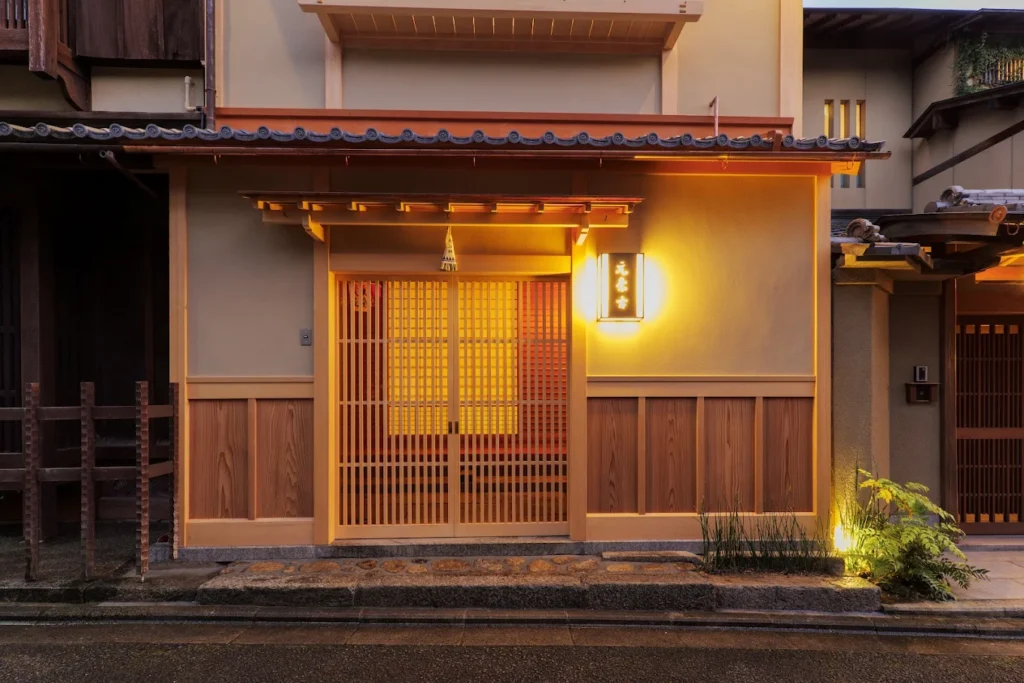 Traditional exterior entrance of Ryokan Motonago in Kyoto, featuring warm lantern lighting, wooden sliding doors, and classic Japanese ryokan architecture in Gion.