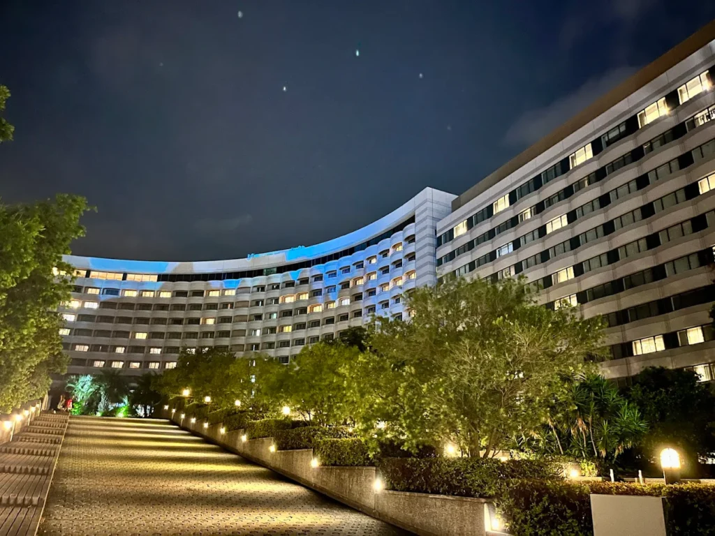 Night view of Sheraton Grande Tokyo Bay Hotel with illuminated pathways, landscaped gardens, and the curved hotel facade glowing under the evening sky near Tokyo DisneySea.