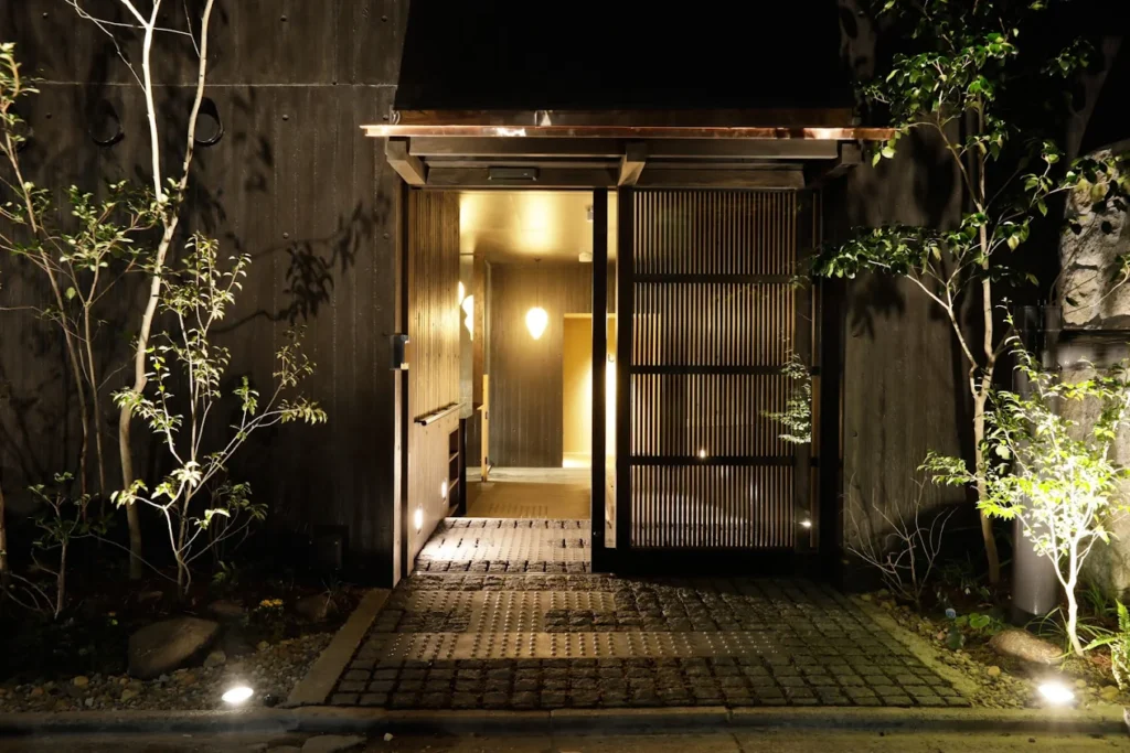 Entrance of Sowaka Kyoto illuminated at night, featuring a traditional wooden facade, stone pathway, and serene Japanese-style lighting in Gion.