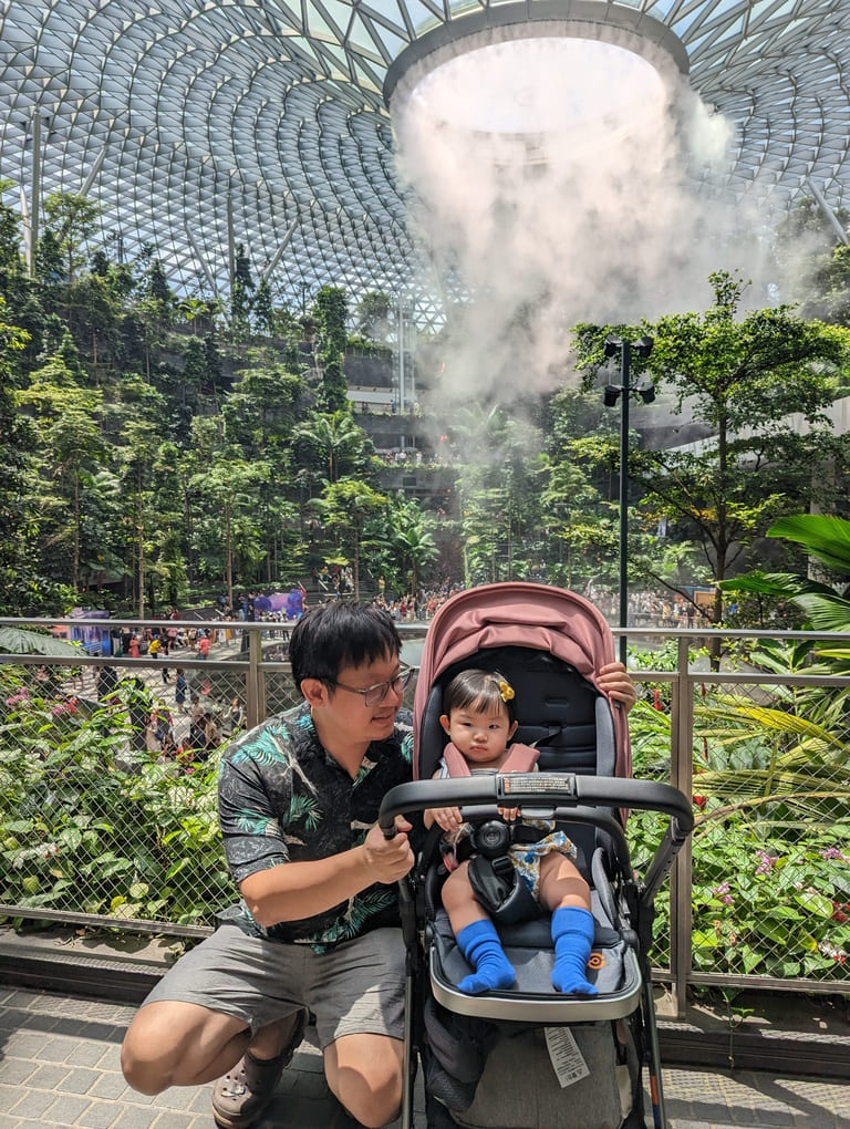 Visiting the Jewel Rain Vortex Singapore: Tips, Photos & What to Expect 6 Father with baby in stroller beside the Jewel Rain Vortex indoor waterfall at Jewel Changi Airport Singapore.