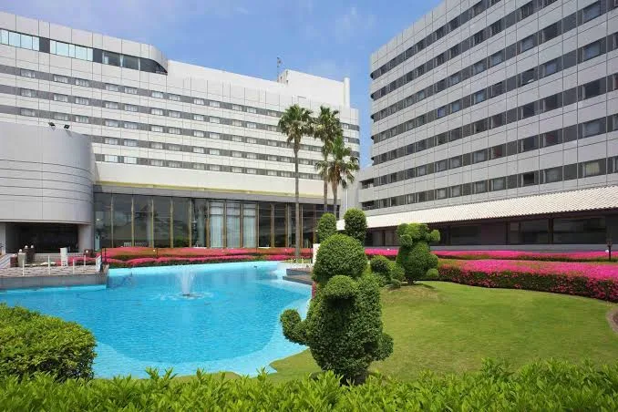 Outdoor pool and landscaped garden area at Tokyo Bay Maihama Hotel First Resort featuring modern hotel buildings, palm trees, fountains, and greenery near Tokyo DisneySea.