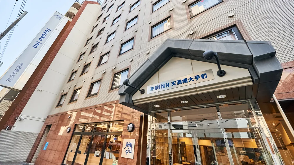 Exterior entrance view of Toyoko Inn Temmabashi Otemae in Osaka, featuring a modern budget hotel facade with glass doors and signage along a city street.