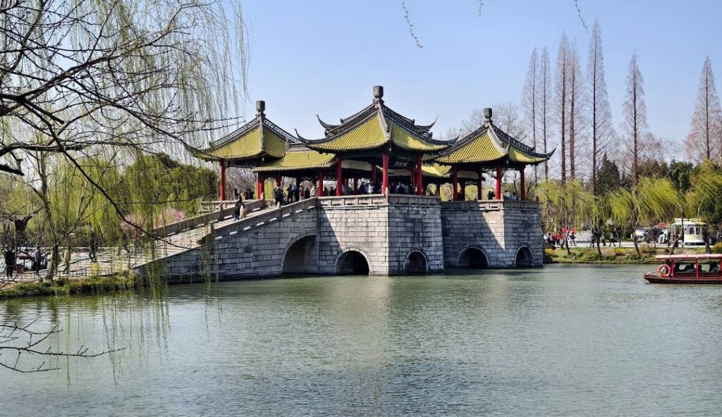 7 Underrated Cities in China Worth Visiting With Your Family 5 Traditional Chinese pavilion bridge over a lake in Yangzhou, Jiangsu, surrounded by willow trees and spring scenery