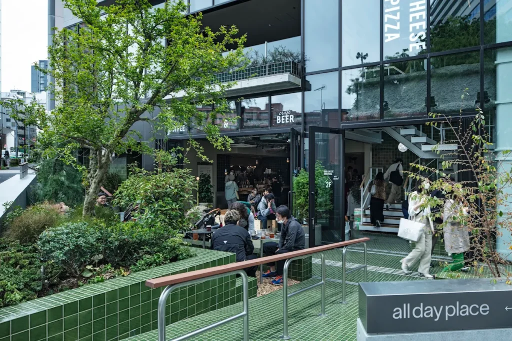 Outdoor entrance area of all day place shibuya with greenery, cafe seating, and modern urban design in Tokyo.