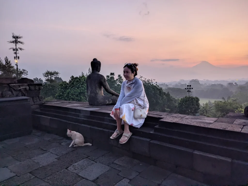 Woman sitting beside Buddha statue during sunrise at Borobudur Temple