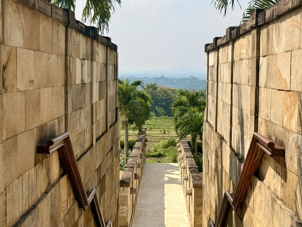 Amanjiwo Review: Is This Luxury Resort Near Borobudur Worth It? 11 Stone corridor walkway at Amanjiwo resort with views of palm trees and rice fields in Java