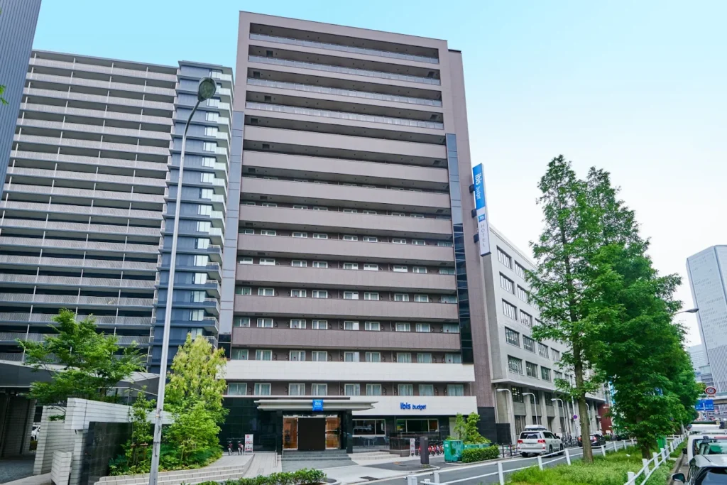 Exterior view of ibis Budget Osaka Umeda hotel near Umeda Station with surrounding high-rise buildings and greenery