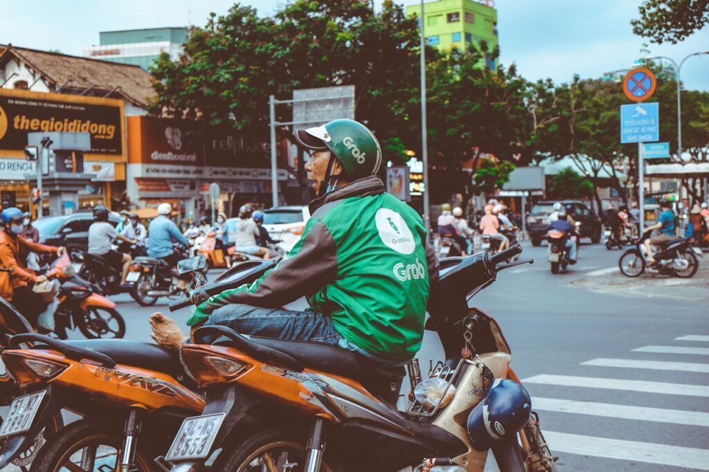 How to Get From Da Nang to Hoi An: Taxi, Bus, Motorbike & Transfer Guide 8 Grab motorbike rider waiting at a busy street intersection in Vietnam, surrounded by scooters and city traffic during daytime.