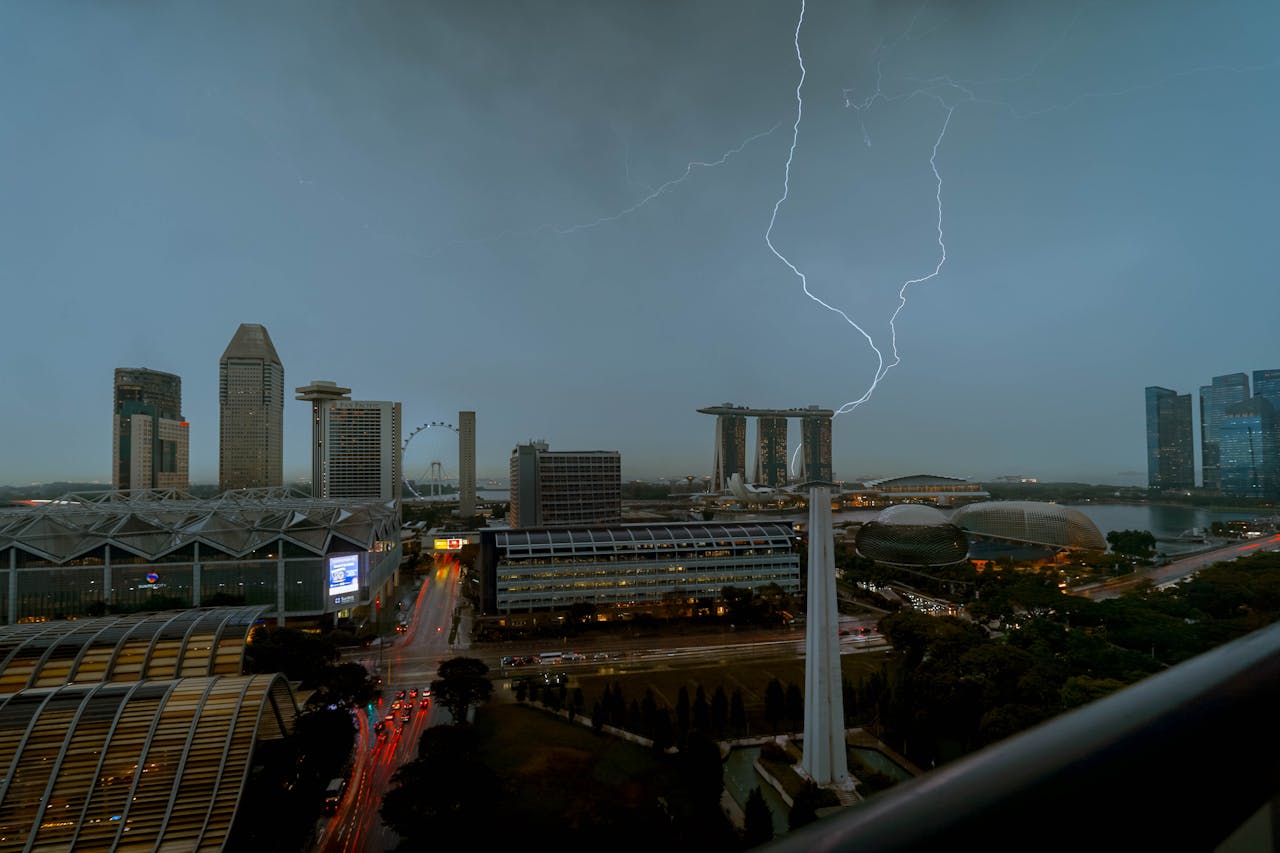 Lightning striking across the Singapore skyline near Marina Bay Sands during a thunderstorm at dusk.