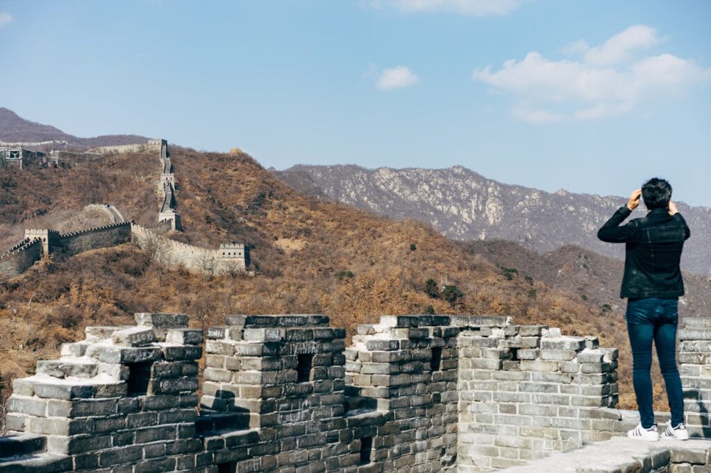 Tourist standing on the Great Wall of China overlooking mountainous landscape under clear blue sky