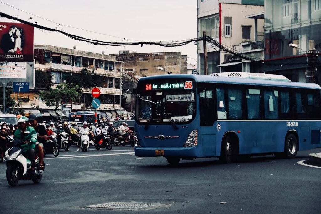 How to Get From Da Nang to Hoi An: Taxi, Bus, Motorbike & Transfer Guide 7 Public bus driving through a busy street intersection in Vietnam, surrounded by motorbikes and urban traffic.