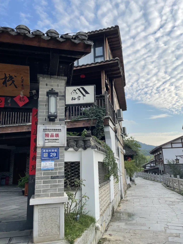 Qingyan Ancient Town Guide: Food, Night Views & Where to Stay 7 raditional wooden guesthouse and stone walkway in Qingyan Ancient Town, Guizhou under a dramatic cloudy sky.