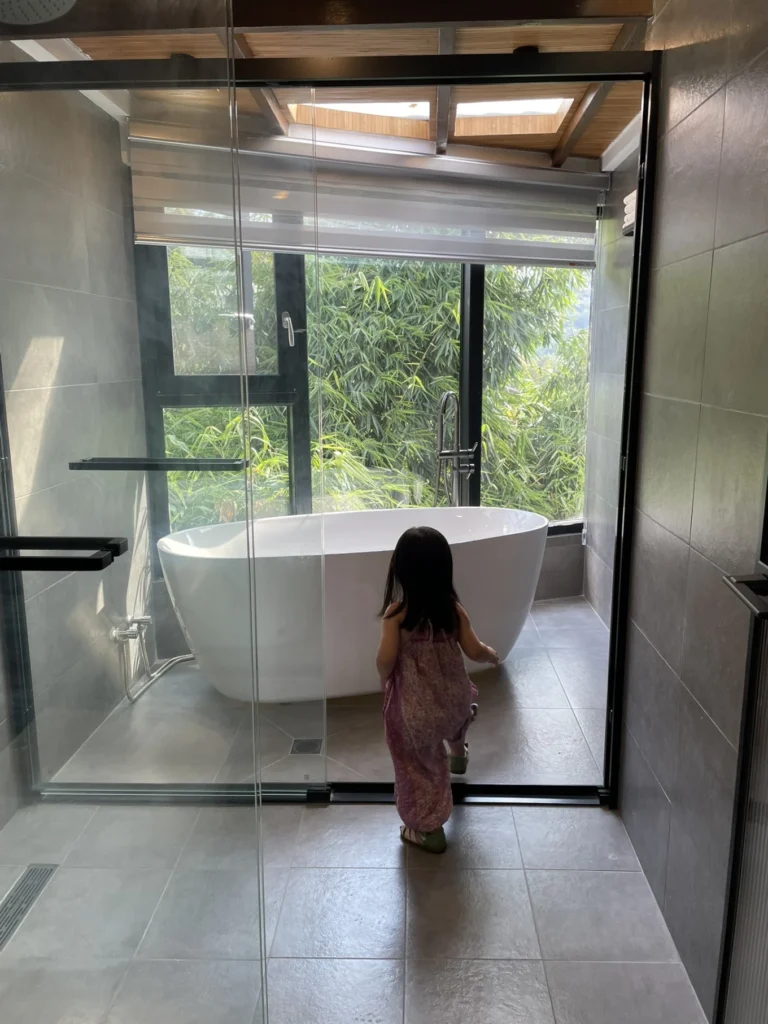 Qishe Inn Review: Cozy Family Stay Near Qingyan Ancient Town 9 Child walking toward freestanding bathtub with bamboo view at Qishe Inn bathroom