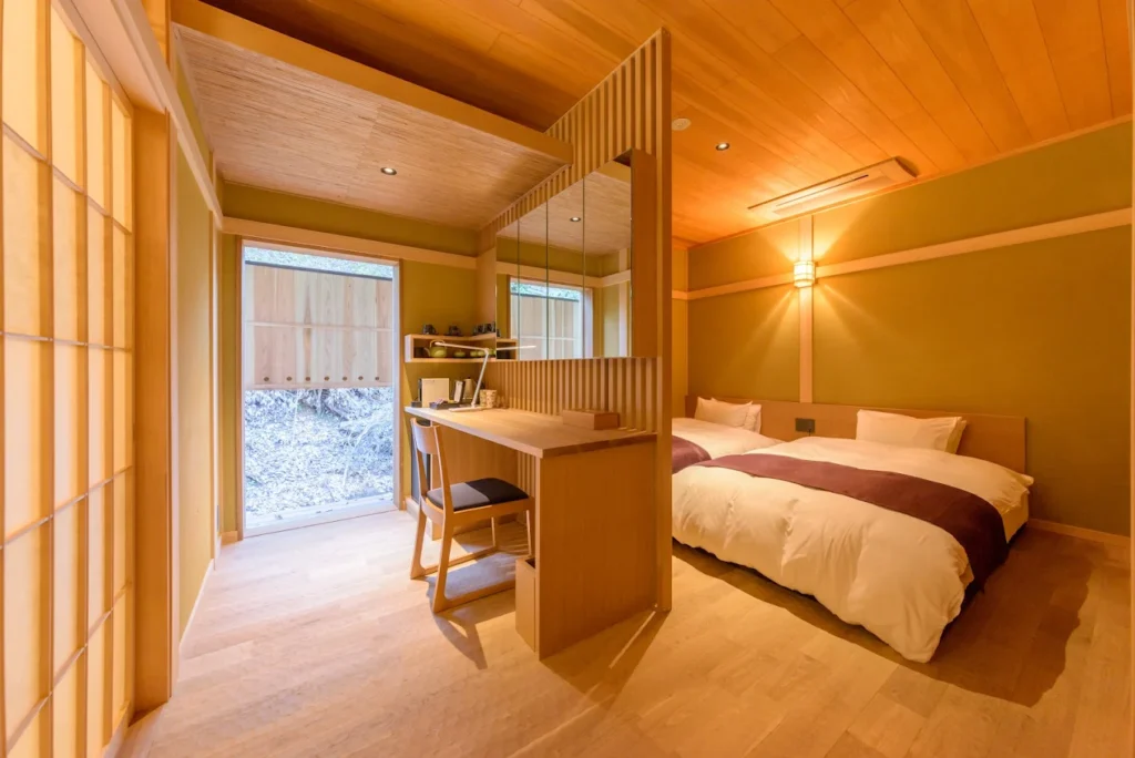 Modern Japanese-style guest room at Hanaikada Ryokan in Arashiyama, featuring warm wooden interiors, twin beds, shoji-inspired design elements, and a tranquil atmosphere.