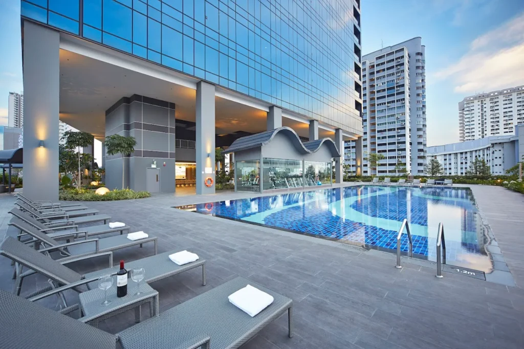 Outdoor swimming pool and leisure deck at Hotel Boss Singapore, featuring sun loungers, modern hotel architecture, and surrounding city buildings.