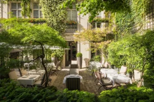Lush private courtyard garden at Hôtel Pavillon de la Reine in Le Marais, Paris, with outdoor seating surrounded by greenery.